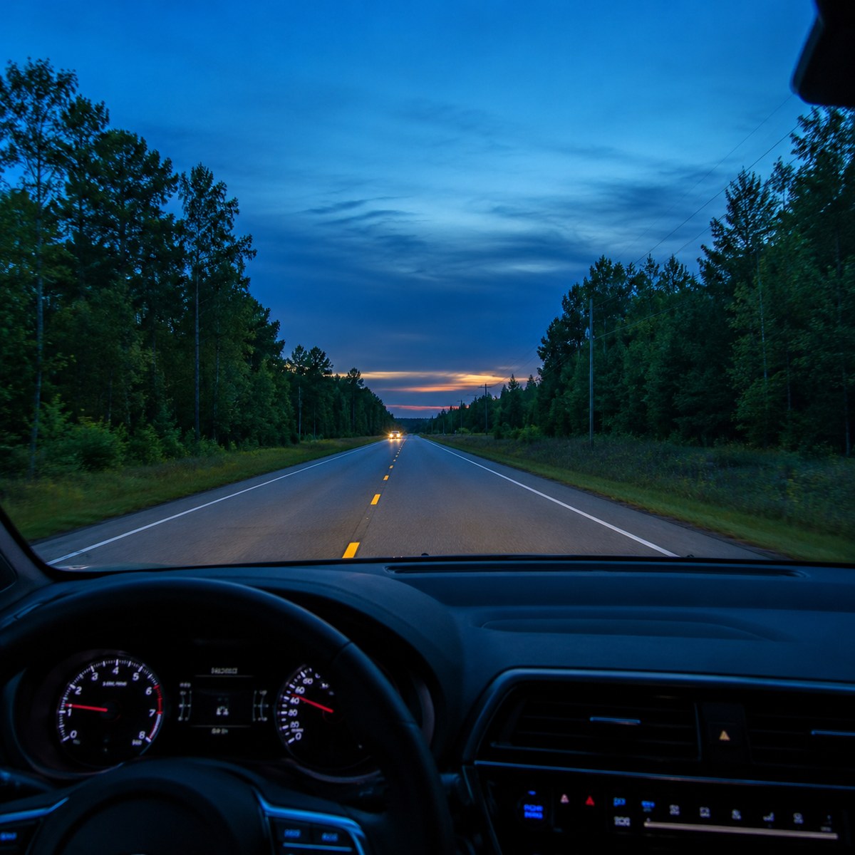 A night road seen through a windshield with clear, controlled headlights.